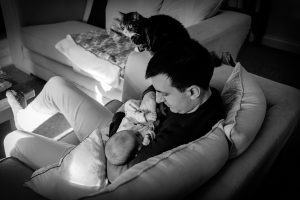 Black and white image of a new father holding his daughter at home in the post natal period