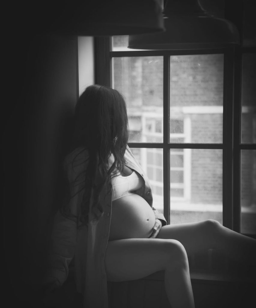 Black and white image of a pregnancy women looking out of a window Erika Townend Birth