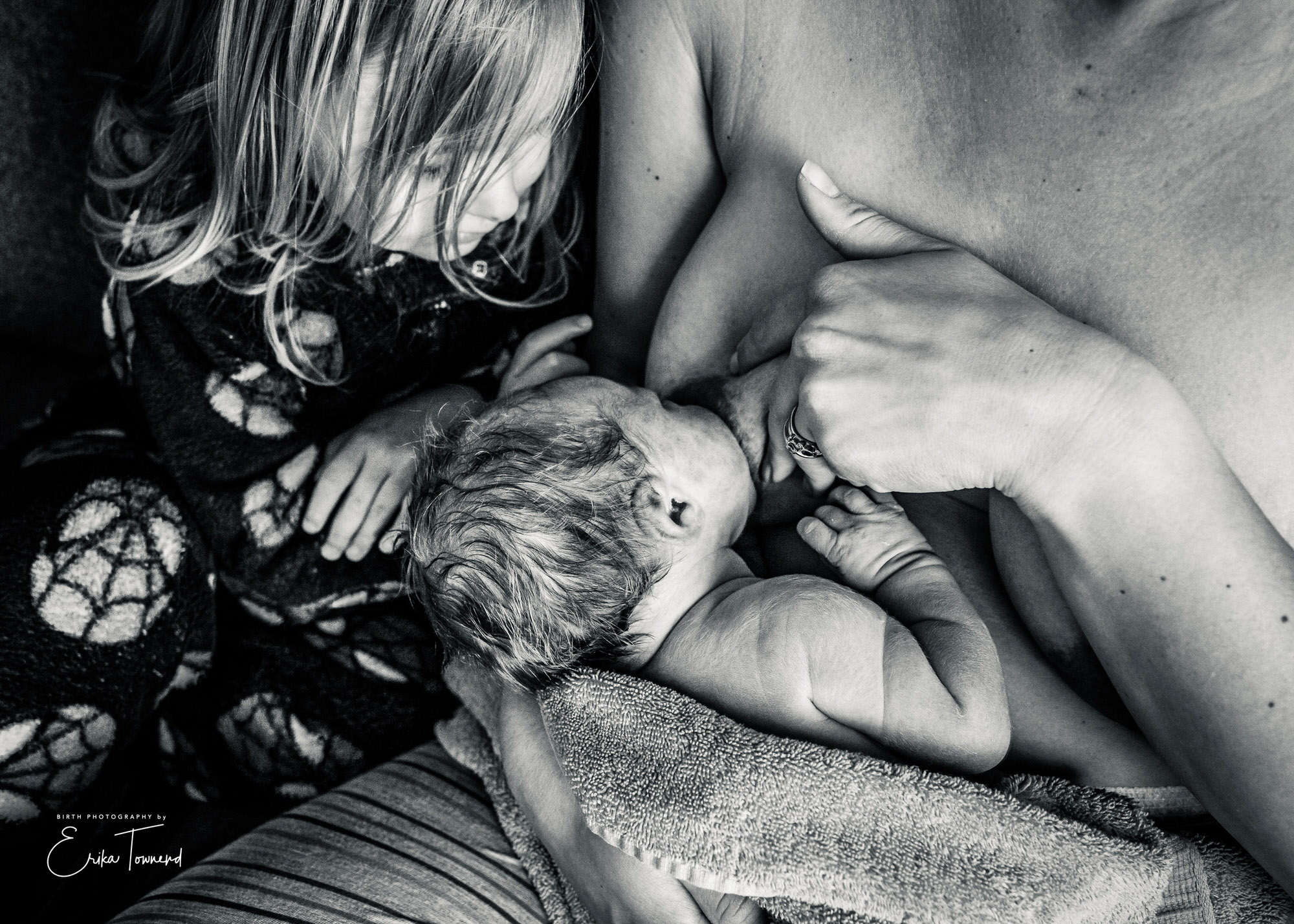 Black and white image of newborn with mother breastfeeding with her first child getting to know her baby sister Birth Photography in Berkshire and Surrey