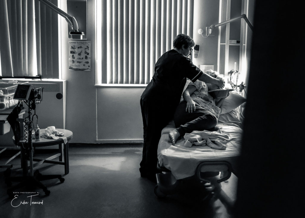 Black and white image of a midwife offering comfort measures at a natural twin birth at a hospital labour by Erika Townend Birth